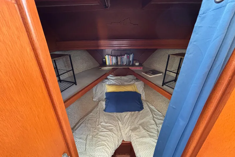 Cozy cabin interior of 1974 Skookum 34 sailboat with bed, books, and shelves.