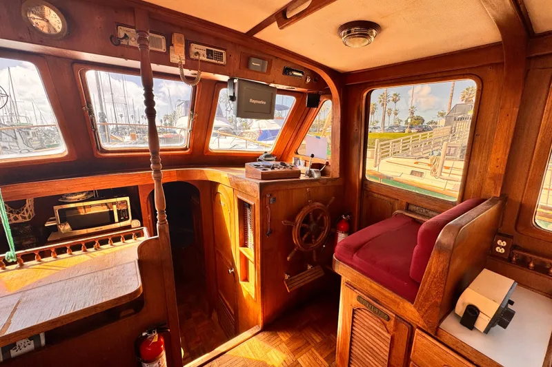 1980 Hershine Trawler interior with wooden helm, vintage equipment, and marina view.