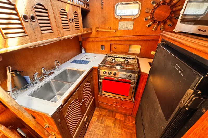 1980 Hershine Trawler kitchen with wooden cabinets, stove, sink, and refrigerator.
