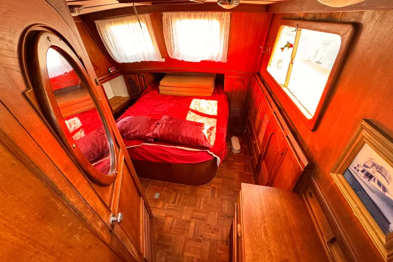 Cozy 1980 Hershine Trawler cabin with wooden interior and red bedding.