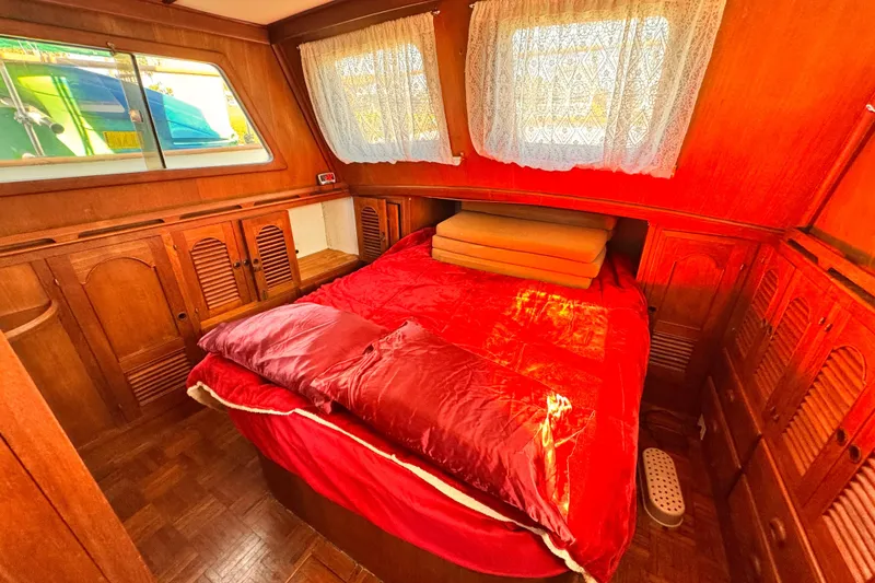 Cozy cabin interior of a 1980 Hershine Trawler with wooden furnishings and red bedding.
