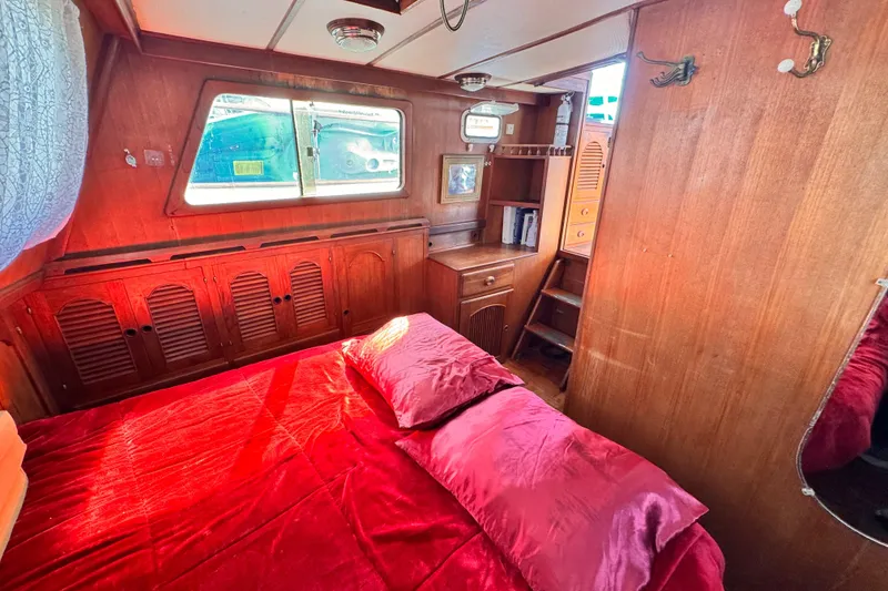 Cozy 1980 Hershine Trawler cabin with red bedding and wooden interior.