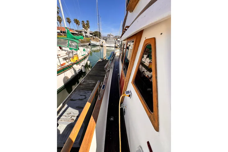 1980 Hershine Trawler docked at marina, side view with wooden accents and nearby sailboats.