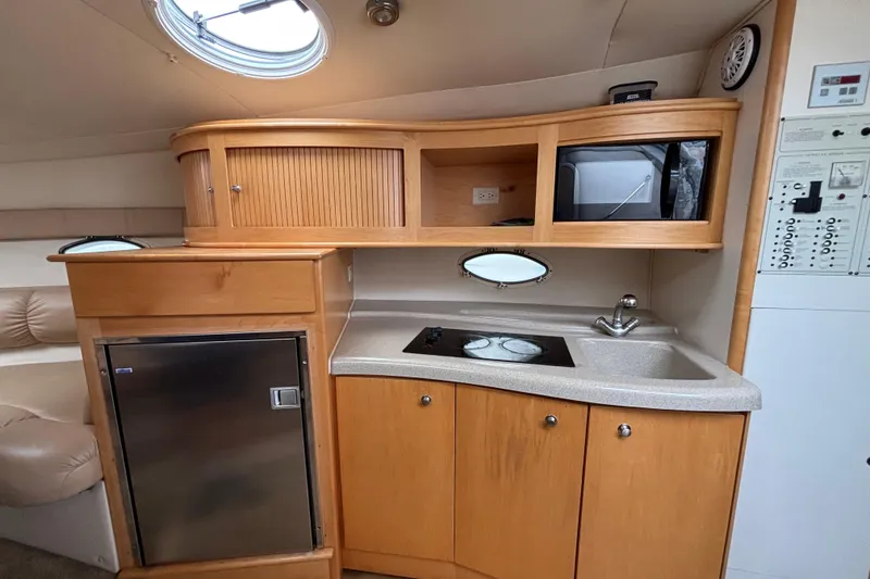 2004 Larson 310 boat interior kitchen with wooden cabinets, sink, stove, and refrigerator.