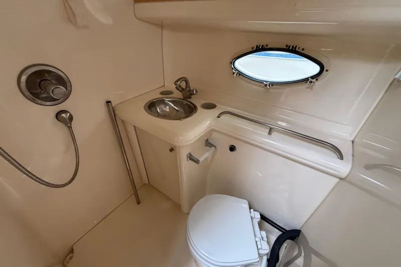2004 Larson 310 boat bathroom with sink, toilet, and porthole window.