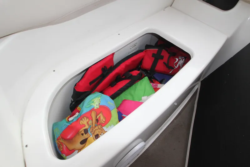 A storage compartment on a boat with life jackets and colorful cushions.