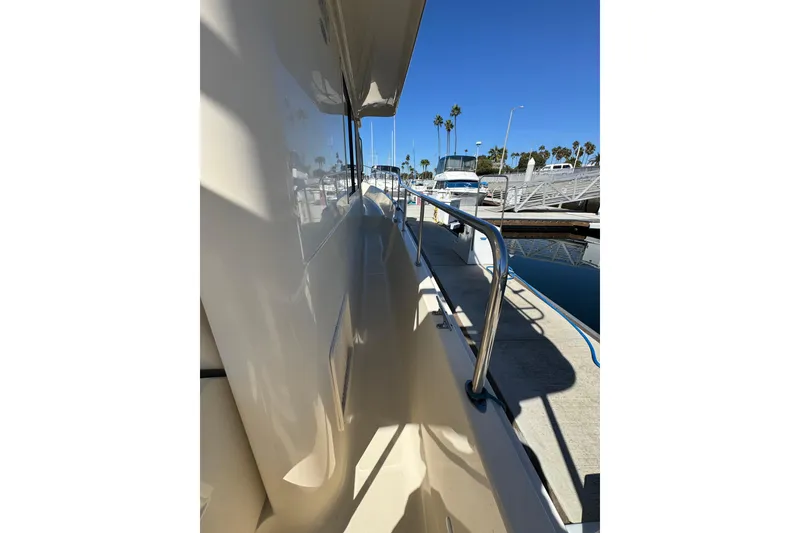 2006 Mainship 34 Trawler side deck view at marina, clear blue sky.