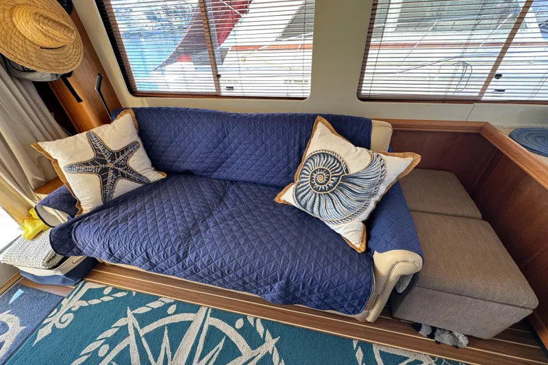 Cozy interior of 2006 Mainship 34 Trawler with nautical-themed pillows and blue quilted sofa.