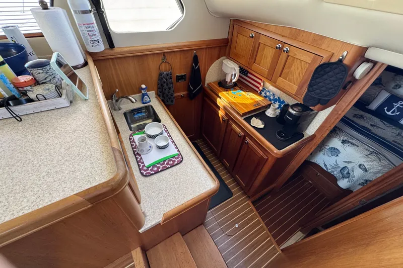 2006 Mainship 34 Trawler kitchen with wooden cabinetry, sink, and countertop accessories.