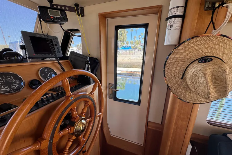 2006 Mainship 34 Trawler helm with wooden wheel, navigation instruments, and straw hat.