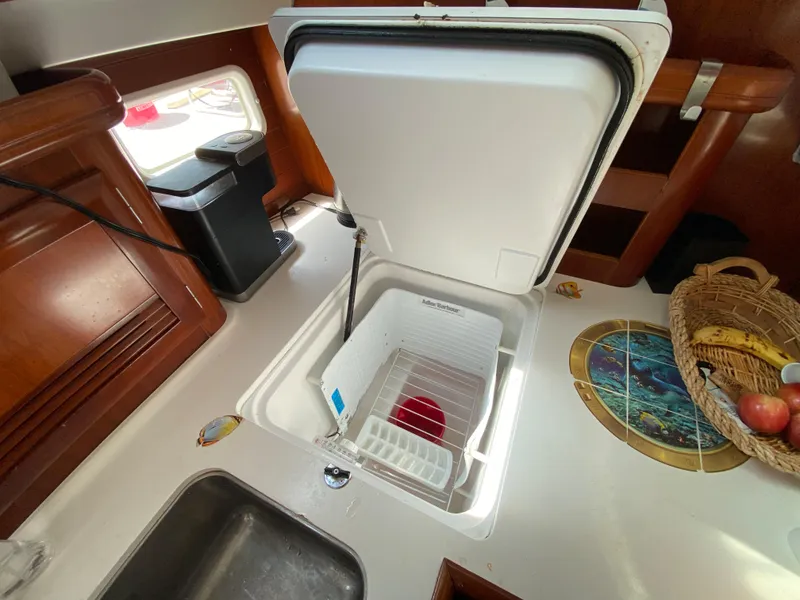 Galley of 2003 Beneteau 423 sailboat with open fridge, sink, and fruit basket.