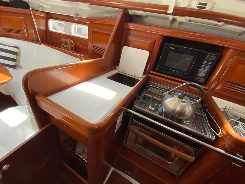 2003 Beneteau 423 yacht kitchen with stove, microwave, and wooden cabinetry.