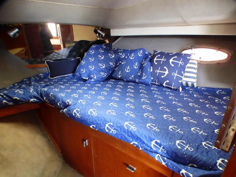 1989 Tiara Yachts 3300 cabin with anchor-themed bedding and wooden storage cabinets.