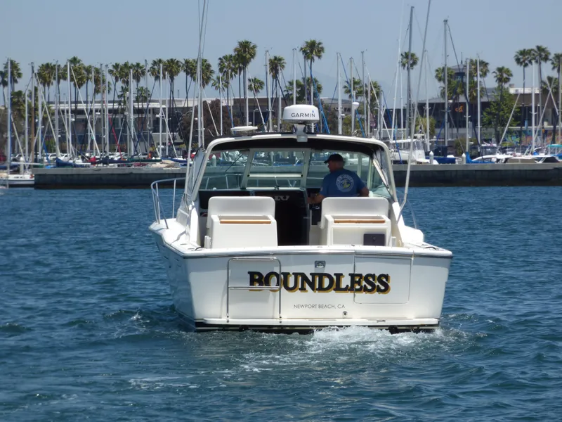1989 Tiara Yachts 3300 boat named "Roundless" cruising in a marina with palm trees.