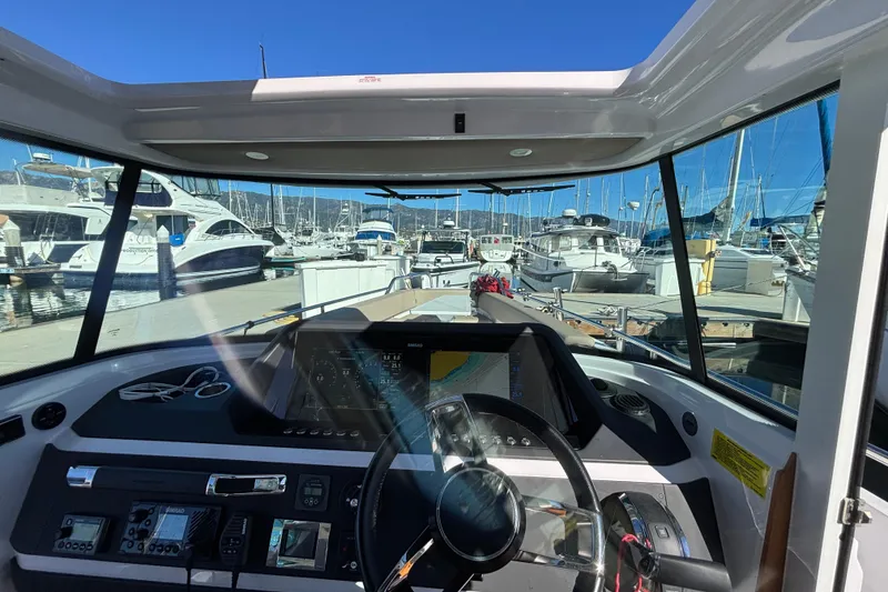 Interior view of 2022 Axopar 28 AFT CABIN boat at marina, showcasing dashboard and steering.