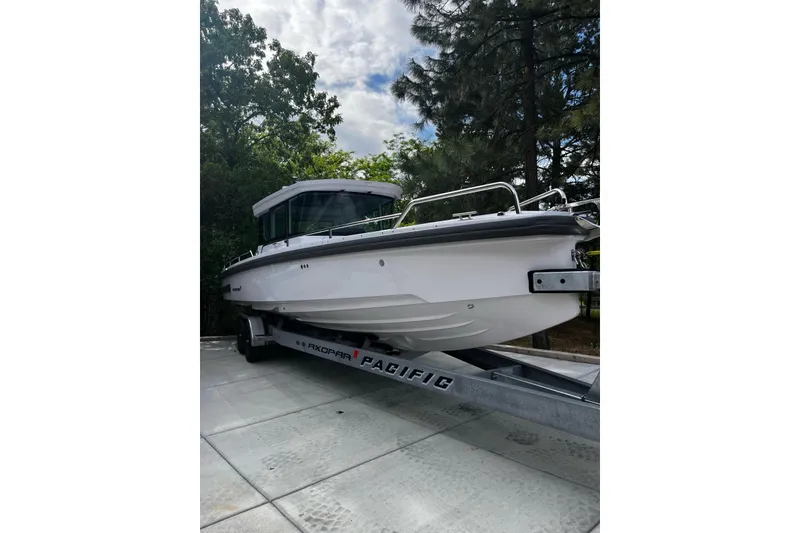 2022 Axopar 28 AFT CABIN boat on trailer, surrounded by trees and cloudy sky.