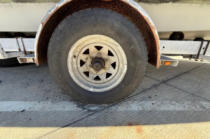 Rusty trailer wheel of a 1996 C-Dory 22 boat on concrete surface.