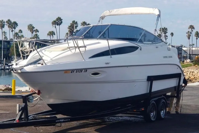 2000 Bayliner 2655 Ciera Sunbridge boat on trailer, dockside with palm trees in background.