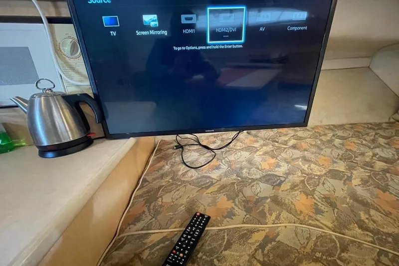 TV setup inside 2000 Bayliner 2655 Ciera Sunbridge, with remote and kettle nearby.