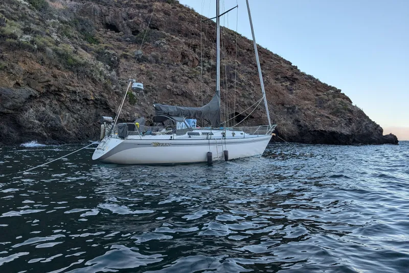 Sailboat Islander Peterson 40 (1979) anchored near rocky coastline, calm waters.