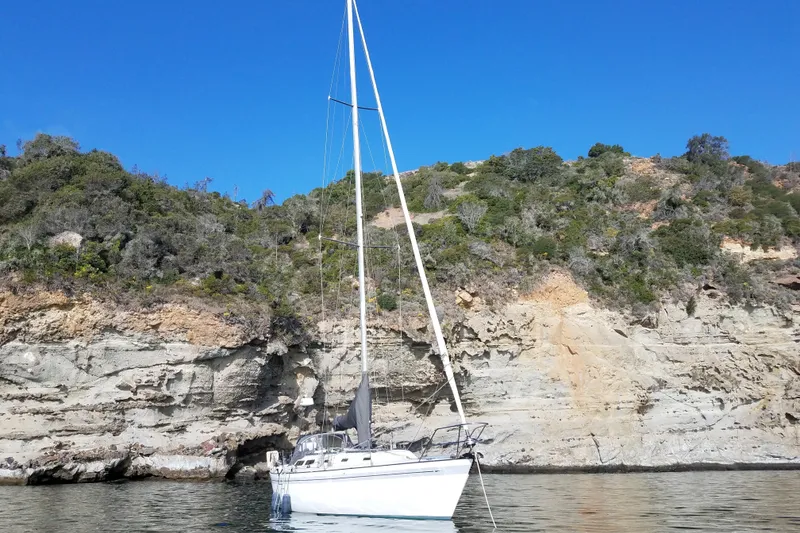 Sailboat Islander Peterson 40 (1979) anchored near rocky coastline under clear blue sky.