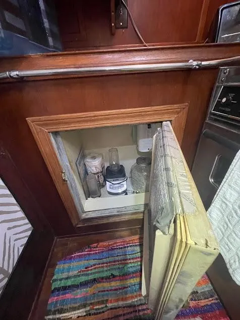 Storage compartment in 1981 Endeavour 43 Center Cockpit Ketch with colorful rug and kitchen items.