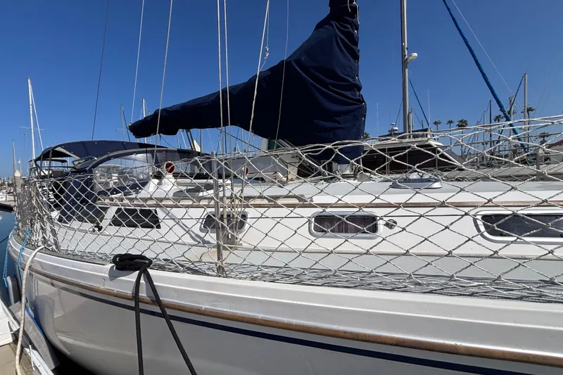 1990 Catalina 42 sailboat docked, featuring netting and covered sails under clear blue sky.