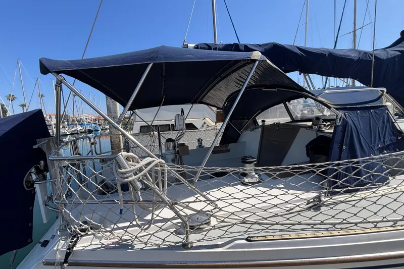 1990 Catalina 42 sailboat with blue canopy docked at marina under clear sky.