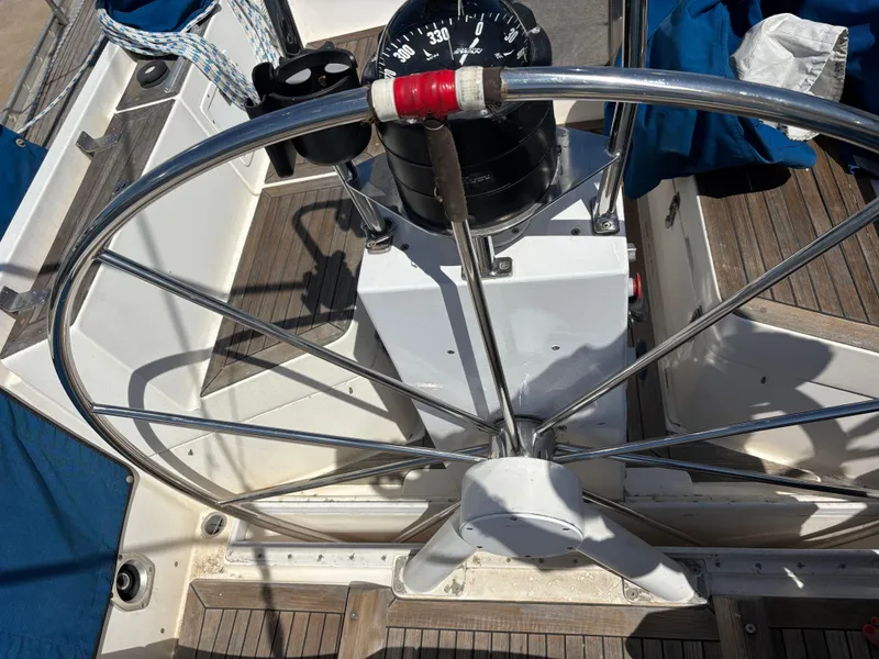 Steering wheel of 1994 Nautor Swan 46 MK II yacht with compass and wooden deck.