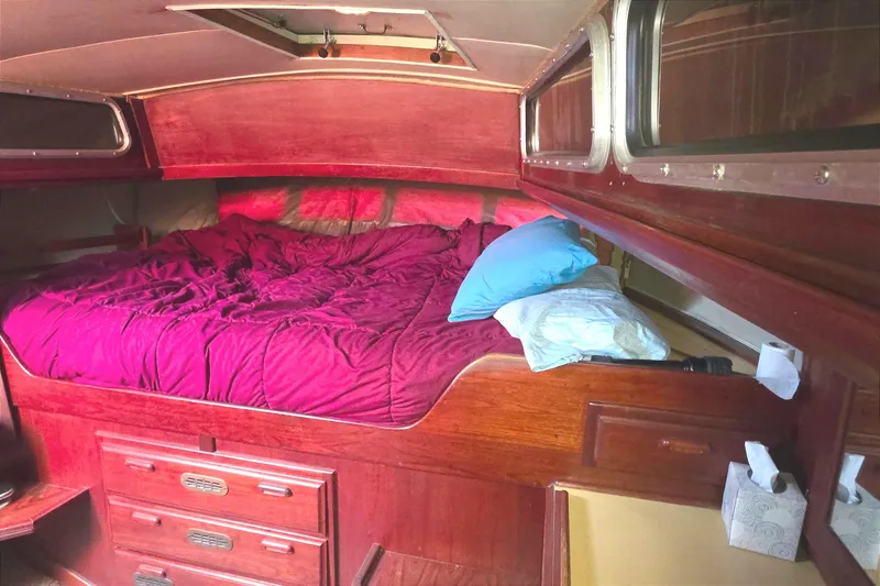 Cozy cabin interior of 1978 Islander Freeport 41 sailboat with red bedding and wooden furnishings.