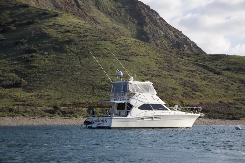 2004 Riviera 47 Flybridge yacht anchored near a scenic, mountainous coastline.