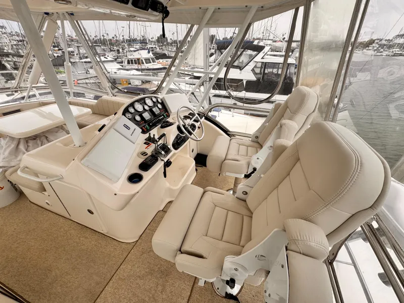 2004 Riviera 47 Flybridge helm with beige seats and control panel, docked in marina.