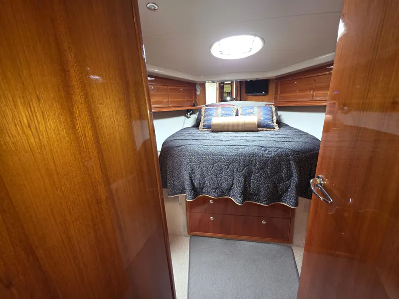 Luxurious cabin interior of 2004 Riviera 47 Flybridge yacht with cozy bed and wooden finish.