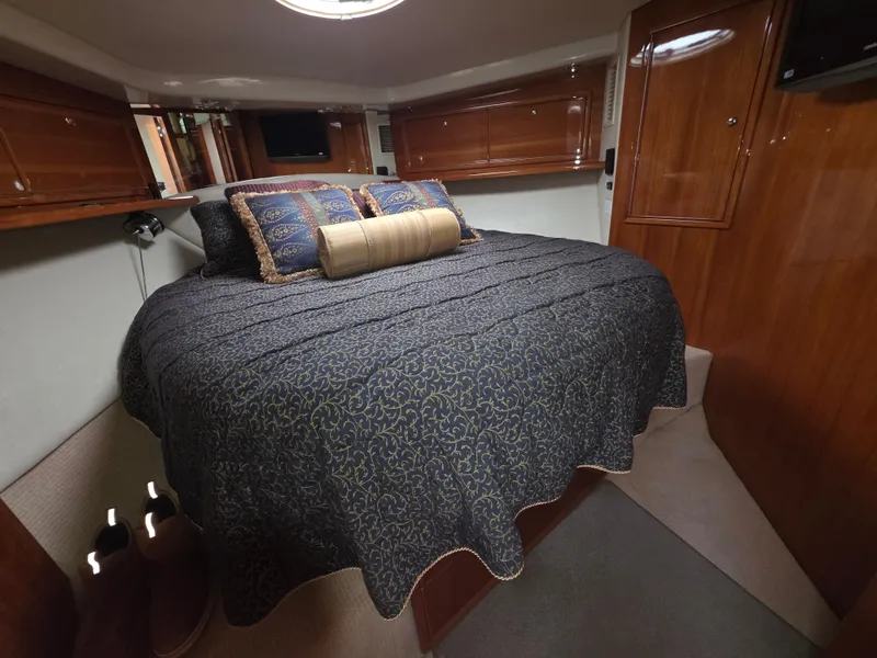 Luxurious bedroom interior of 2004 Riviera 47 Flybridge yacht with elegant bedding and wood paneling.