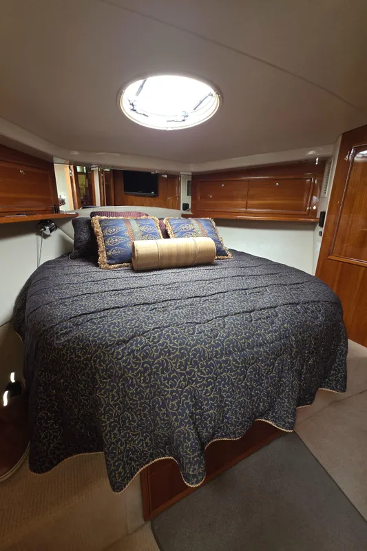 Luxurious bedroom interior of 2004 Riviera 47 Flybridge yacht with elegant bedding and wood accents.