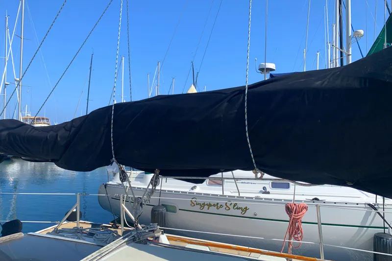 1984 Ericson 30 Plus sailboat docked in marina, covered boom, clear blue sky.