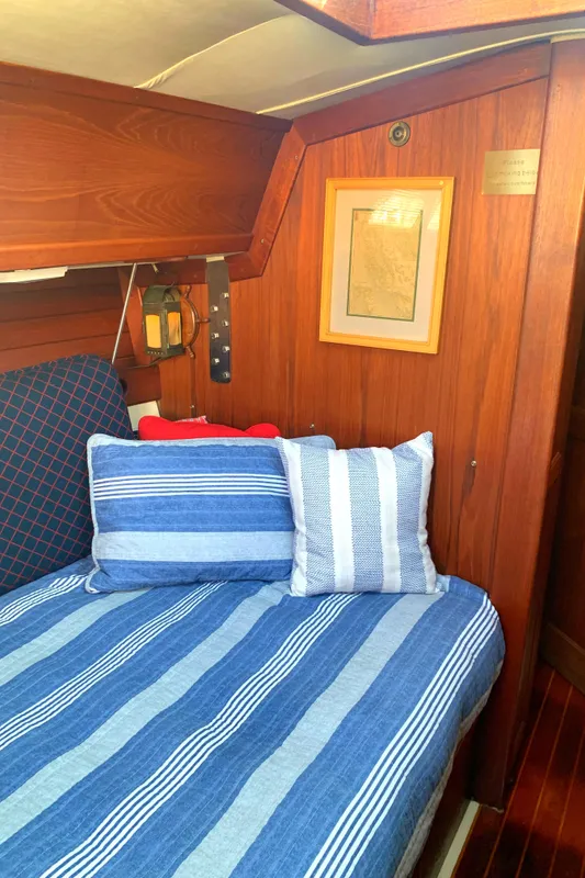 Cozy cabin interior of 1984 Ericson 30 Plus sailboat with striped bedding and wooden paneling.