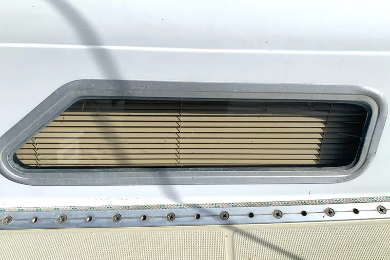 Port window of a 1984 Ericson 30 Plus sailboat with metal frame and blinds.