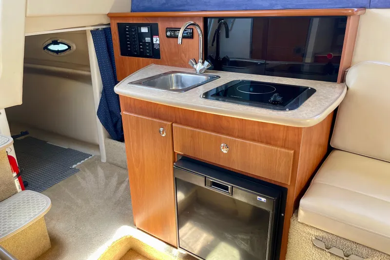 2008 Bayliner 265 boat interior with kitchenette, featuring sink, stove, and mini-fridge.