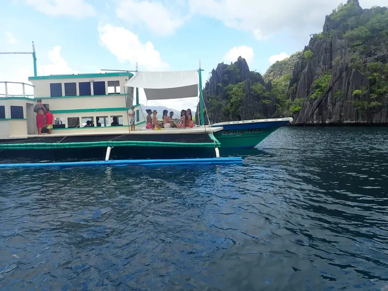 Phinisi Custom Pleasure Cruiser 2016 on scenic water with passengers, rocky cliffs in background.