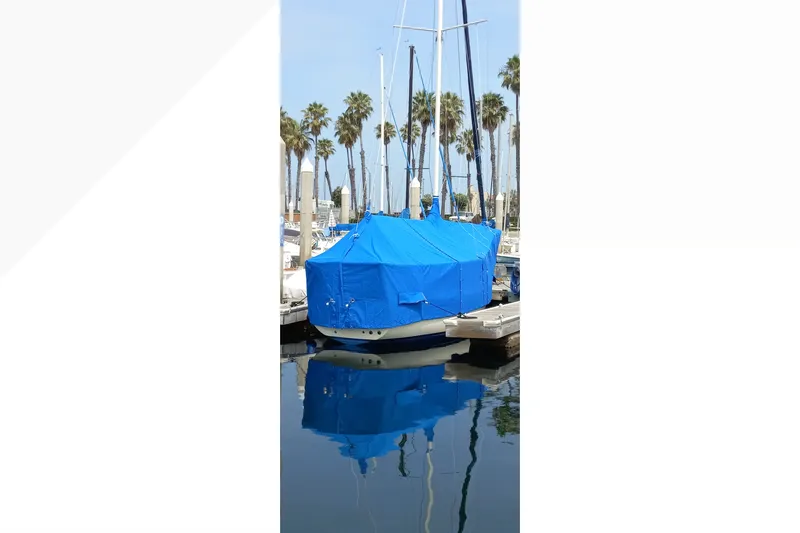 Blue-covered 2002 Pacific Seacraft Dana 24 sailboat docked, reflecting in calm marina waters.