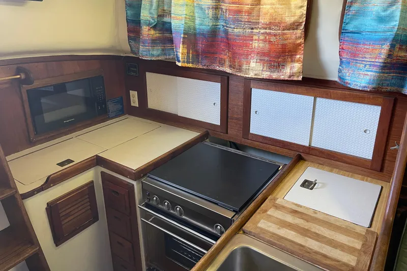1978 Downeast 38 boat kitchen with stove, microwave, and colorful curtains.