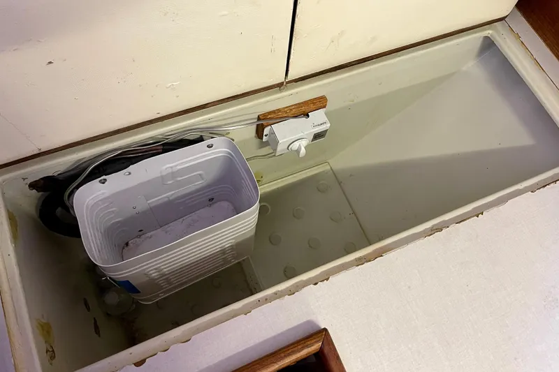 Storage compartment in a 1978 Downeast 38 boat with a white container and wiring.