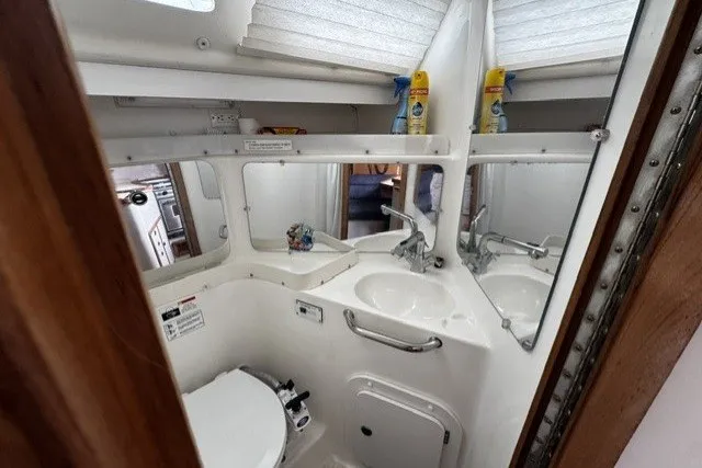 Compact bathroom in a 2000 Catalina 320 sailboat, featuring a sink, toilet, and mirror.