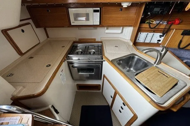 Compact kitchen in a 2000 Catalina 320 sailboat with stove, sink, and microwave.