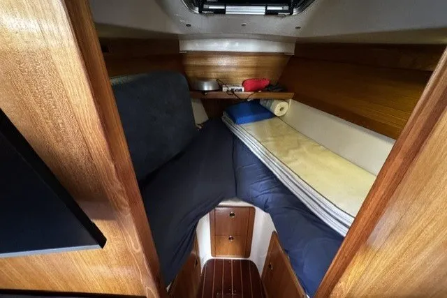 Cozy cabin interior of a 2000 Catalina 320 sailboat with wooden finishes and bedding.