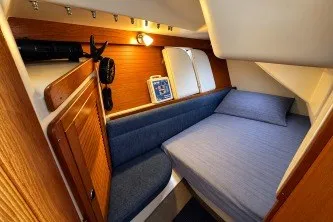 Cozy cabin interior of a 2000 Catalina 320 sailboat with wooden accents and blue bedding.
