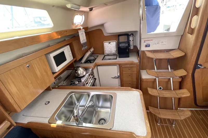 2004 Catalina 350 yacht interior kitchen with wooden cabinetry, stainless steel sink, and appliances.