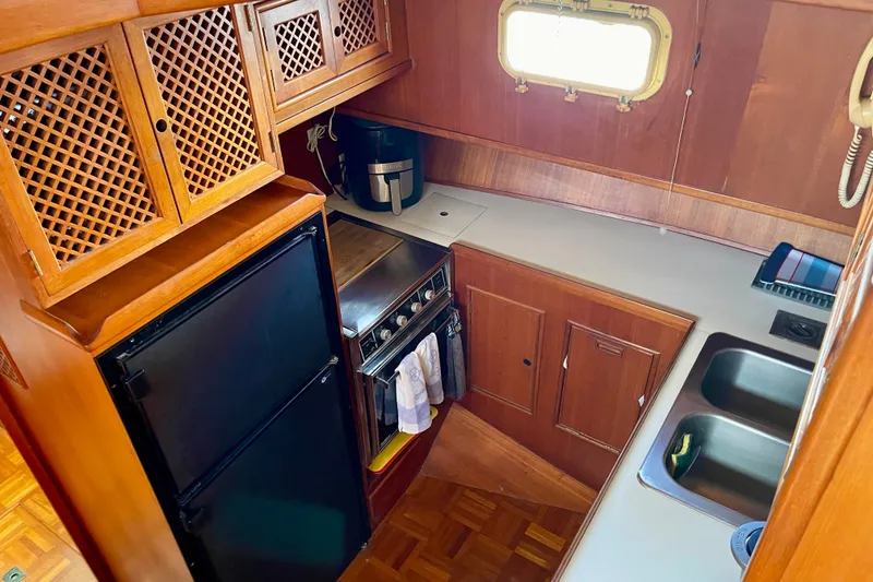Compact kitchen in a 1985 CHB 42 boat with wooden cabinetry and modern appliances.