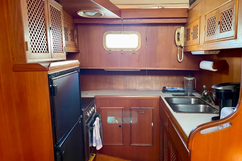 1985 CHB 42 yacht kitchen with wooden cabinets, stove, sink, and window.